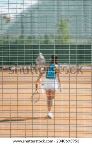 Close up of focused net with blurred figure of girl playing tennis on sunny day, sport background