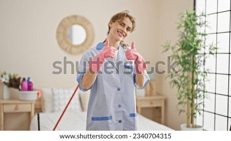 Young woman professional cleaner wearing gloves doing thumbs up gesture at bedroom