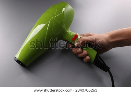 Woman hand holds bright green hair dryer on gray background Royalty-Free Stock Photo #2340705263
