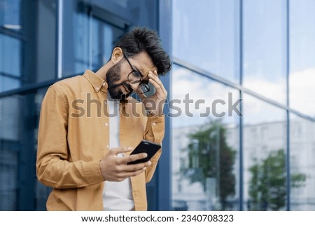 Upset businessman received message with bad news, hispanic man outside office alarm clock cheated and bankrupt, man unhappy with achievement results walking in city. Royalty-Free Stock Photo #2340708323