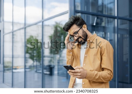 Upset businessman received message with bad news, hispanic man outside office alarm clock cheated and bankrupt, man unhappy with achievement results walking in city. Royalty-Free Stock Photo #2340708325
