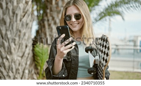 Young blonde woman holding skate using smartphone at park