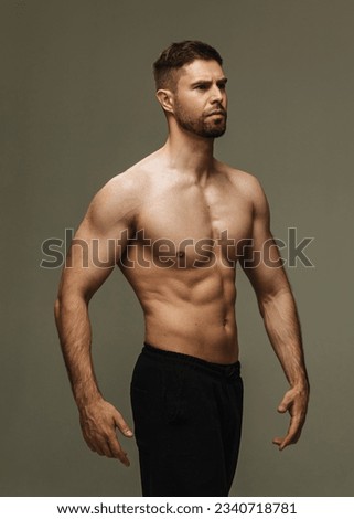Slim muscular male model at gray background. Fitness shirtless guy in black sport pants posing in studio. Royalty-Free Stock Photo #2340718781