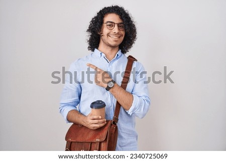 Hispanic man with curly hair drinking a cup of take away coffee cheerful with a smile on face pointing with hand and finger up to the side with happy and natural expression 
