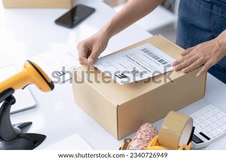 Young woman placing barcode label on top of product box for online business delivery, online sales, package delivery, e-commerce.