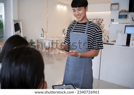 Barista takes orders in coffee shop, uses smartphone and tablet for menu introduction to customers, coffee shop owner.