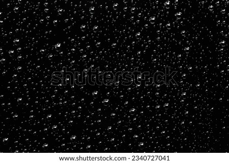 Rain droplets or splashing and floating drop on the black glass at the night, Blurry images of soda liquid water bubbles, sparkling and refreshing Abstract background. Monochrome texture.