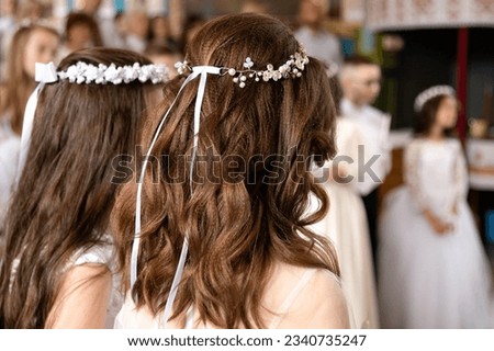 Dark-haired girls with a festive hairstyle and a wreath on their heads are standing in the church. Holy Liturgy. First Communion. Focus delight. CultureOfFaith, Culture Of Faith Royalty-Free Stock Photo #2340735247