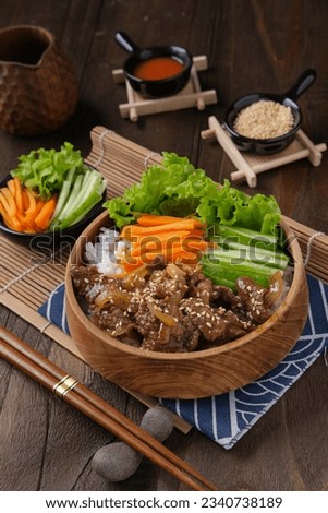 Beef teriyaki rice bowl with garnish of lettuce, sliced carrots, cucumbers, and sprinkled sesame seeds in a wooden bowl. A typical dish from Japan. Photographed from above at a 45-degree angle.