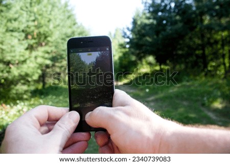 Male hands holding a smartphone in the forest. Close-up.