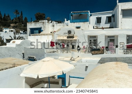 White roofs of Sidi Bou Said with drying laundry on the clothesline, overlooking a hill and palm trees in the distance Royalty-Free Stock Photo #2340745841