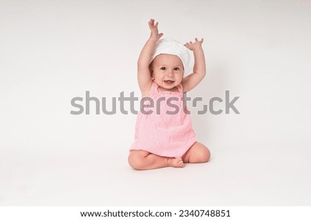 Baby girl sitting on the floor with arms up in the air Royalty-Free Stock Photo #2340748851