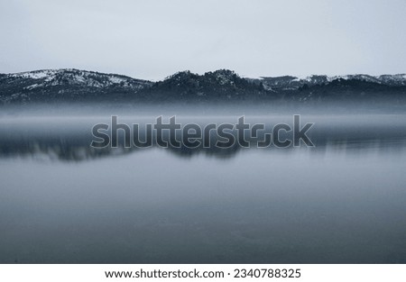 Long exposure shot of the lake at sunrise. Panorama view of the mountains and forest reflection in the water surface in an early morning with fog.  Royalty-Free Stock Photo #2340788325