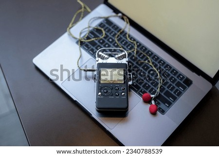 Focus on the voice recorder and earbuds lying on the laptop.