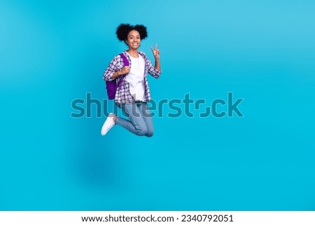 Full length photo of sweet shiny girl dressed checkered shirt jumping showing v-sign going college isolated blue color background