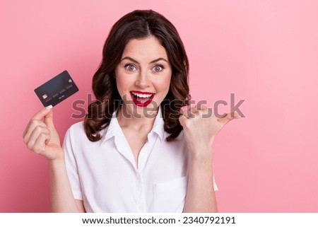 Photo of positive excited woman dressed white shirt showing thumb empty space rising credit card isolated pink color background