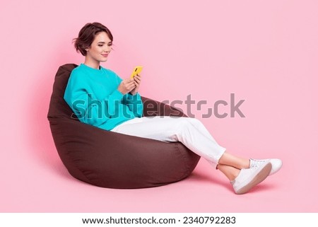 Full size photo of pretty young girl beanbag hold gadget apple samsung android wear trendy blue outfit isolated on pink color background