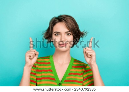 Photo of good mood pretty lady wear striped cardigan pointing two fingers up empty space isolated teal color background