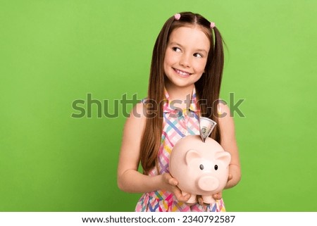 Photo of cute positive schoolkid arms hold money bank pig look empty space isolated on green color background