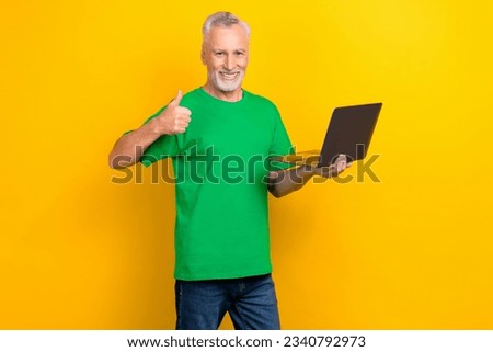 Photo of cheerful grandfather hold netbook hand finger demonstrate thumb up approval isolated on yellow color background