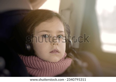 Pensive young girl watching cartoons in headphones while traveling in a car