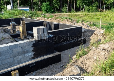 Footings made of concrete blocks painted with black dispersion asphalt-rubber mass, reinforced concrete pillars visible. Royalty-Free Stock Photo #2340796373