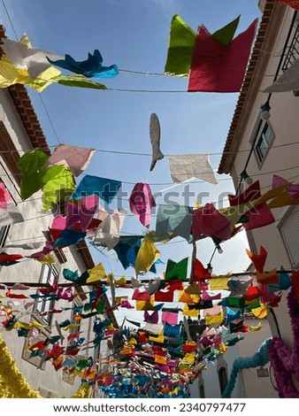 Bright-colored fabric hanging from ropes across a small street to celebrate the Festival of Trays in Portugal. The street sign translates to "Walkway of Saint John".