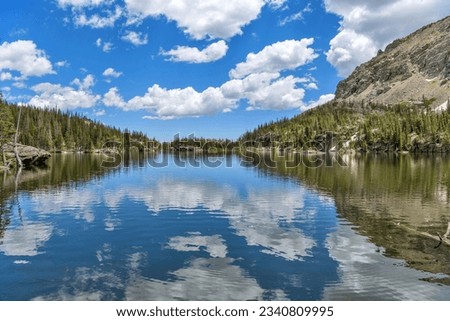The Loch - A summer day view of blue sky and white clouds reflecting in calm mountain lake - The Loch, as seen from west end of the lake towards to its east outlet. Rocky Mountain National Park, CO. Royalty-Free Stock Photo #2340809995