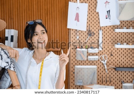 Young clothing designer or stylist stands next to a mannequin in her studio workshop and with pen in hand, she contemplates and sparks new design ideas for her clothes. 