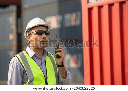 Logistic or engineer foreman talking on radio phone or walkie-talkie with colleague in container warehouse. inspecting for quality control. shipping delivery and export import concept