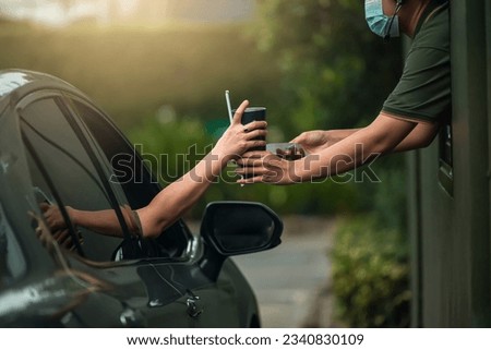 Hand WoMan in car receiving coffee in drive thru fast food restaurant. Staff serving takeaway order for driver in delivery window. Drive through and takeaway for buy fast food for protect covid19.