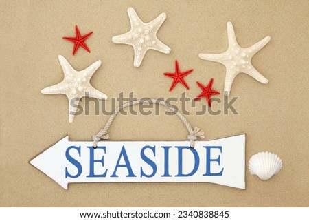 Seaside sign with starfish and cockle shell on sand background.