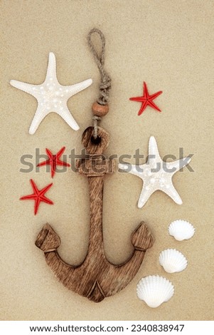 Starfish and cockle shells with decorative anchor on beach sand background.