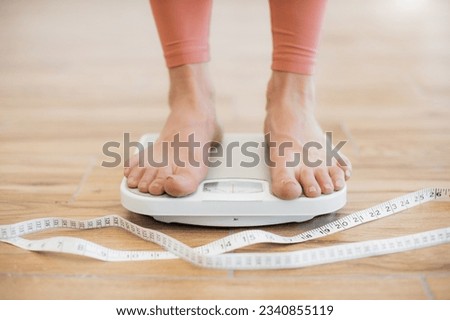 Close up view of barefoot human legs in tight-fitting terracotta pants standing on mechanical scales on wooden floor. Athletic person going through weight control check after body tape measurement.