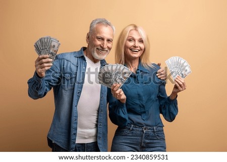 Lottery, giveaway, cashback, gambling concept. Thrilled positive elderly couple happy man and woman enjoying their prize, holding cash money dollar banknotes, isolated on beige background