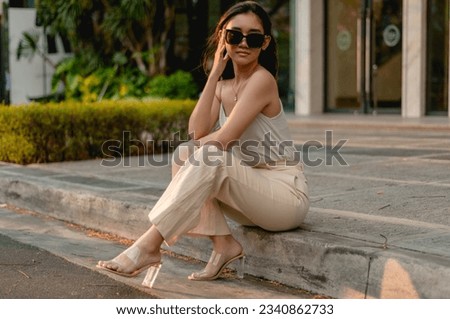 A young classy asian woman in a light top and khaki pants and wearing stylish sunglasses at the city mall during the afternoon. Royalty-Free Stock Photo #2340862733