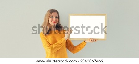 Happy woman decorating interior, hanging white blank photo frame, wooden picture, artwork mockup on wall in new house