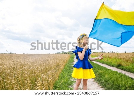 Wrapped in blue yellow flag, girl leaves. child with symbol of Ukraine. Ukrainian girl walks on field.