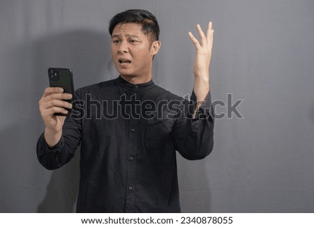 Moslem asian man wearing moslem shirt is upset while holding mobile phone