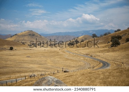 A dry grassland scene with hills, road, and trees