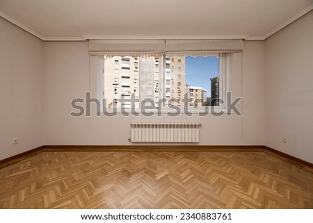 Empty living room with French oak parquet flooring arranged in a herringbone pattern, white aluminum windows with shutters and heating below and views of buildings outside Royalty-Free Stock Photo #2340883761