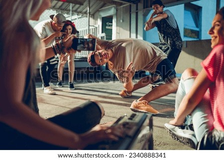 Group of young people break dancing in a parking lot and recording with their smart phone Royalty-Free Stock Photo #2340888341