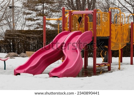 view of a children playground with red slide in winter with snow on the ground