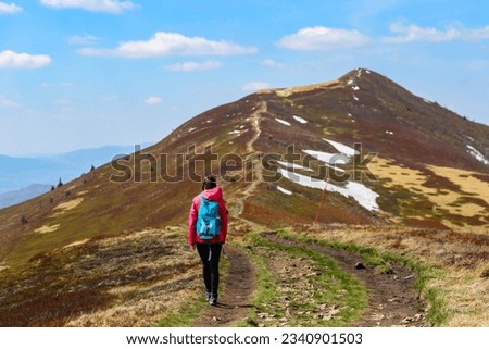 girl in pink jacket walks along a mountain ridge during spring; mountain walk with vegetation coming to life, colourful spring in the mountains	