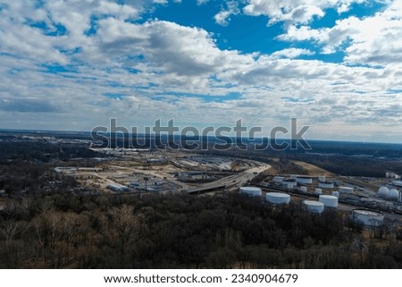 aerial shot of an oil refinery on the banks of the Mississippi River with bare winter trees, flowing water and powerful clouds in Memphis Tennessee USA