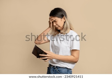 Financial problems. Poor Asian woman holding an empty wallet. She is in debt and has no money isolated on light brown background. Royalty-Free Stock Photo #2340921411