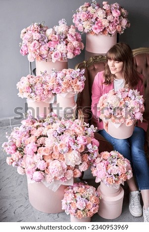 a happy young girl holds a box of flowers in her hands and looks away. A beautiful woman is sitting on a sofa surrounded by flowers. A box with peonies and bush spray roses in a peach-pink range.