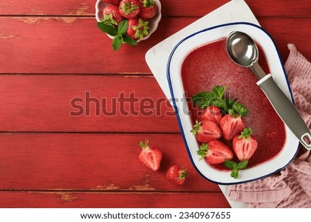 Strawberry granita or fresh berry sorbet in white rustic bowl on old wooden table background. Ice cream with strawberry and mint. Summer treat. Top view.