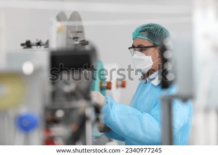 Rear view worker in personal protective equipment or PPE inspecting quality of mask and medical face mask production line in factory, manufacturing industry and factory concept.