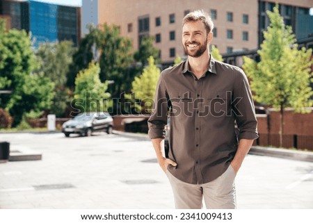 Handsome smiling stylish hipster lambersexual model. Modern man dressed in shirt and trousers. Fashion male posing in the street background. Outdoors at sunny day Royalty-Free Stock Photo #2341009413
